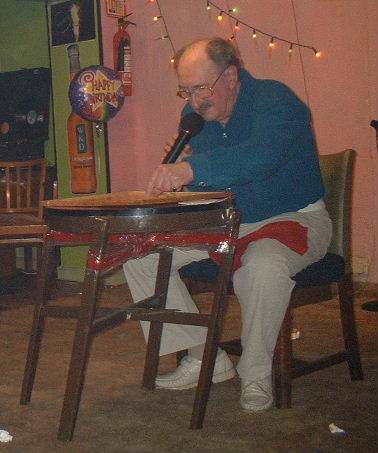 Gordon Cragg seated at a table leaning acutely and held together with sticky tape